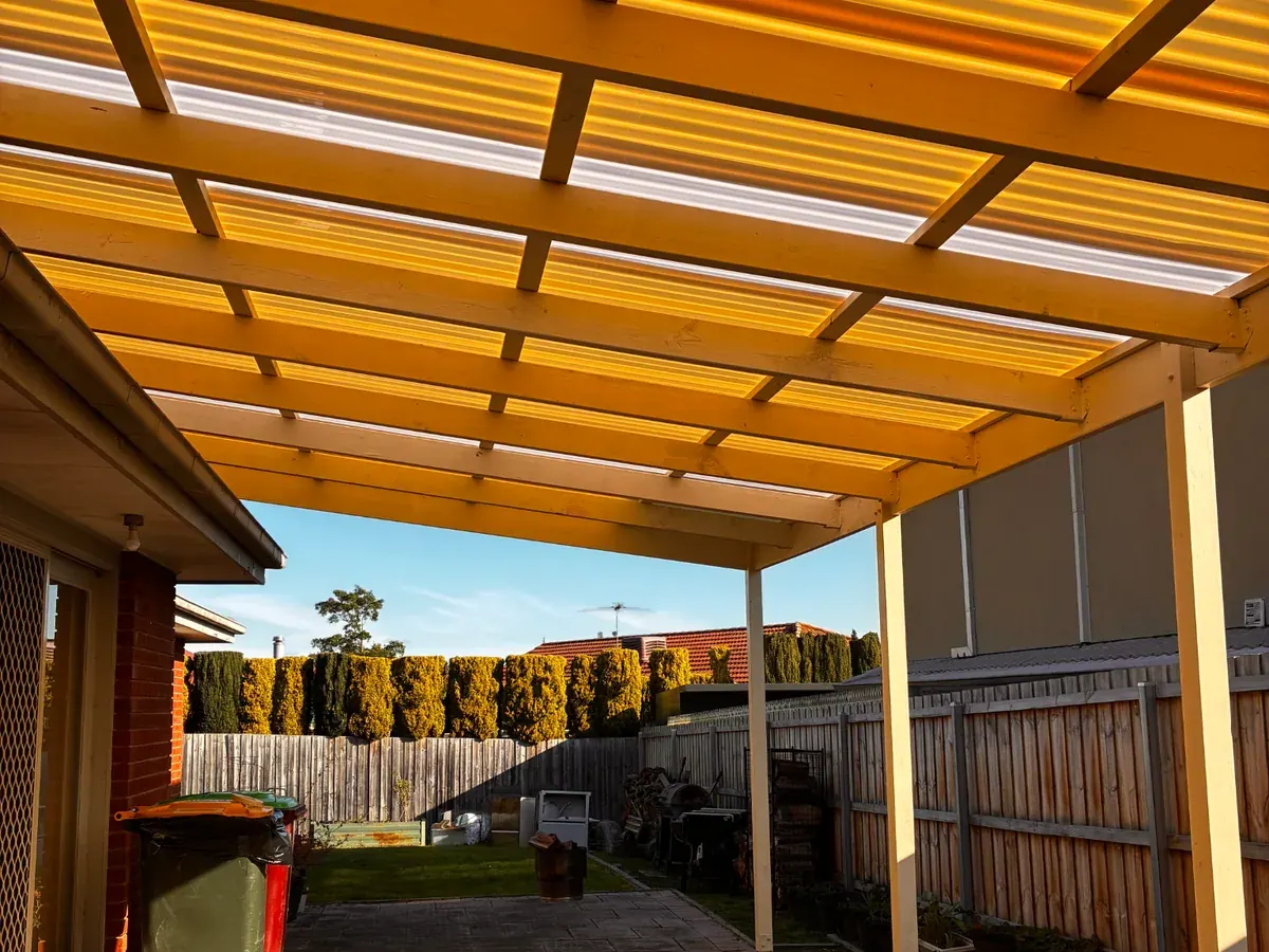 View beneath a pergola roof beside a brick home.